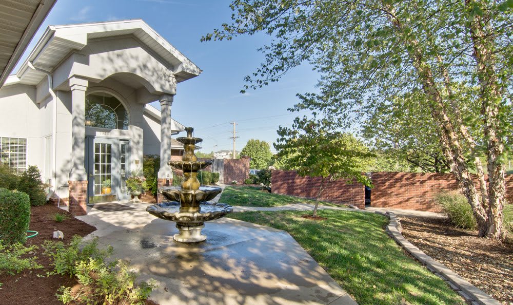 A tranquil patio area with a decorative fountain surrounded by trees and grass.