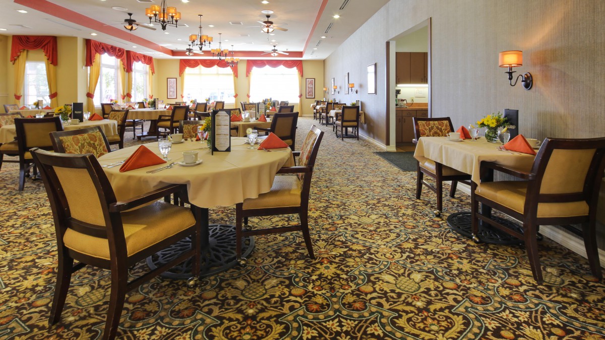 A spacious and elegantly decorated dining room with multiple tables and chairs arranged on a patterned carpet.