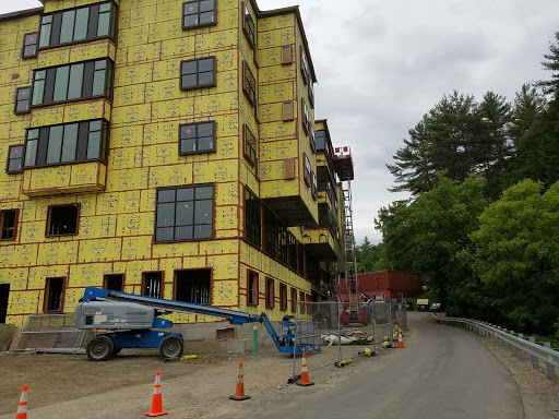 A construction site featuring a partially built multi-story building with yellow insulation and surrounding safety measures.