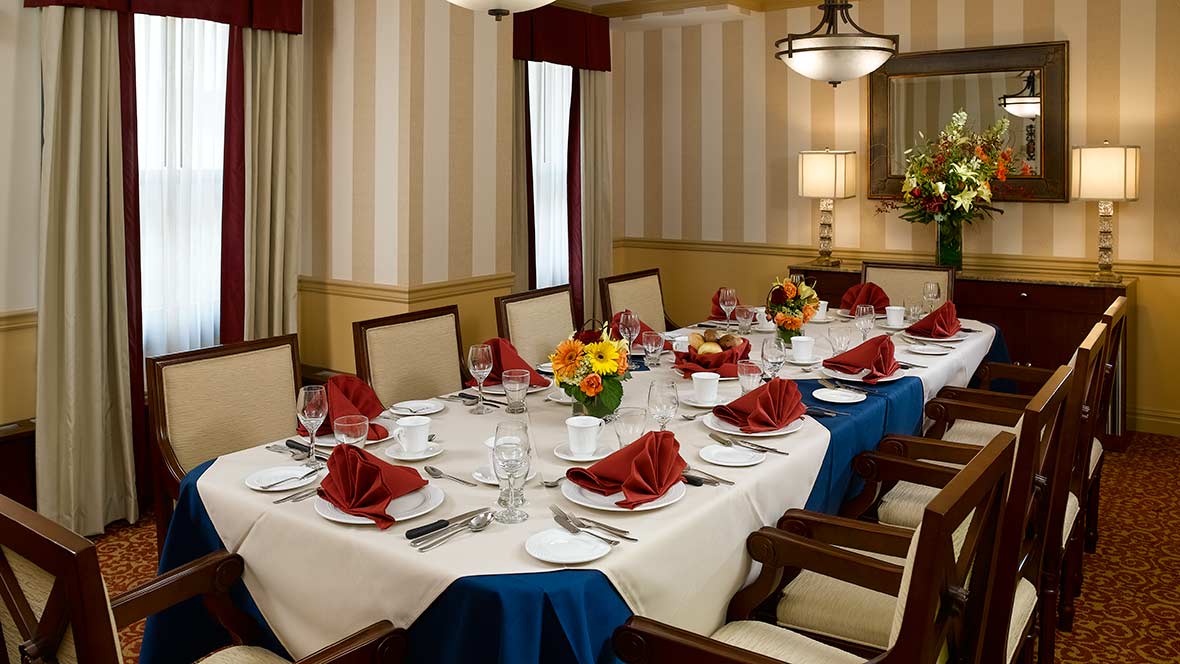 A formal dining room set with an elegantly arranged table, featuring red napkins and floral centerpieces.