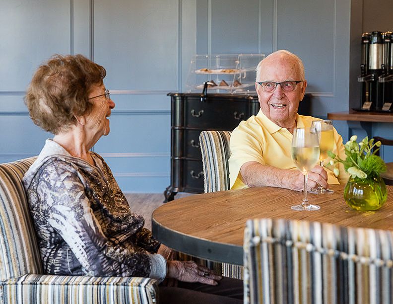 Two seniors enjoying a seated conversation indoors.