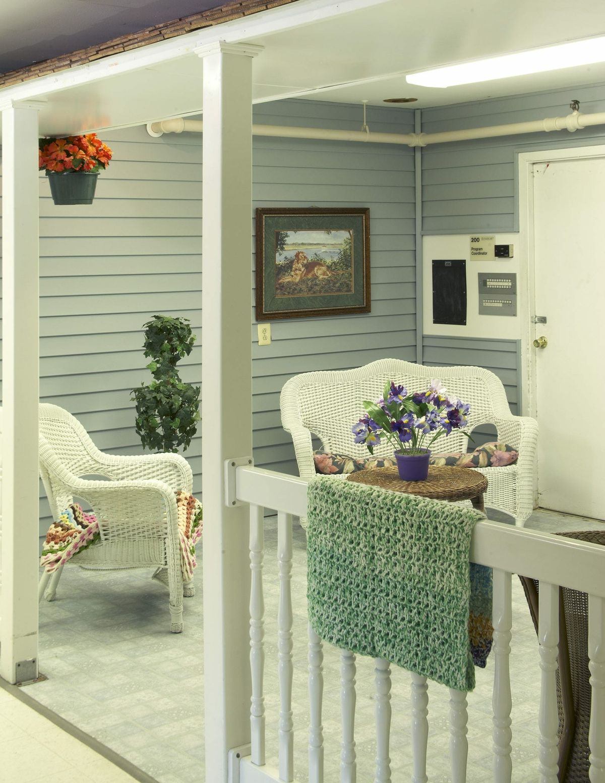 A cozy porch with white wicker furniture, colorful flowers, and a touch of greenery.
