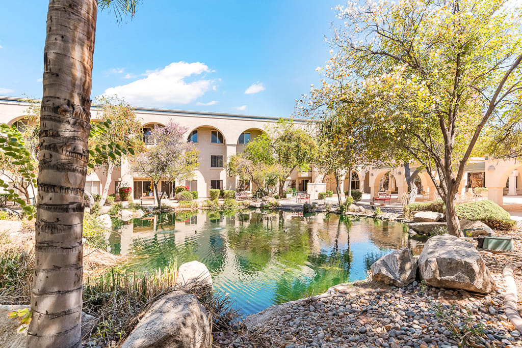 A picturesque view of a building with arches, surrounded by trees and a peaceful pond reflecting the scenery.