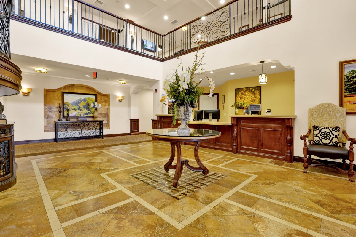 A spacious and elegant hotel lobby with a central table adorned with flowers, featuring warm lighting and classic interior decor.