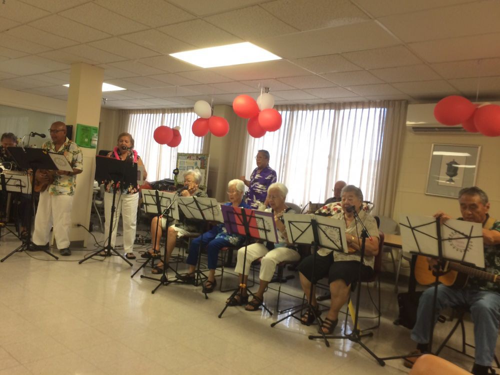 A group of senior musicians performing indoors with music stands and festive balloons.