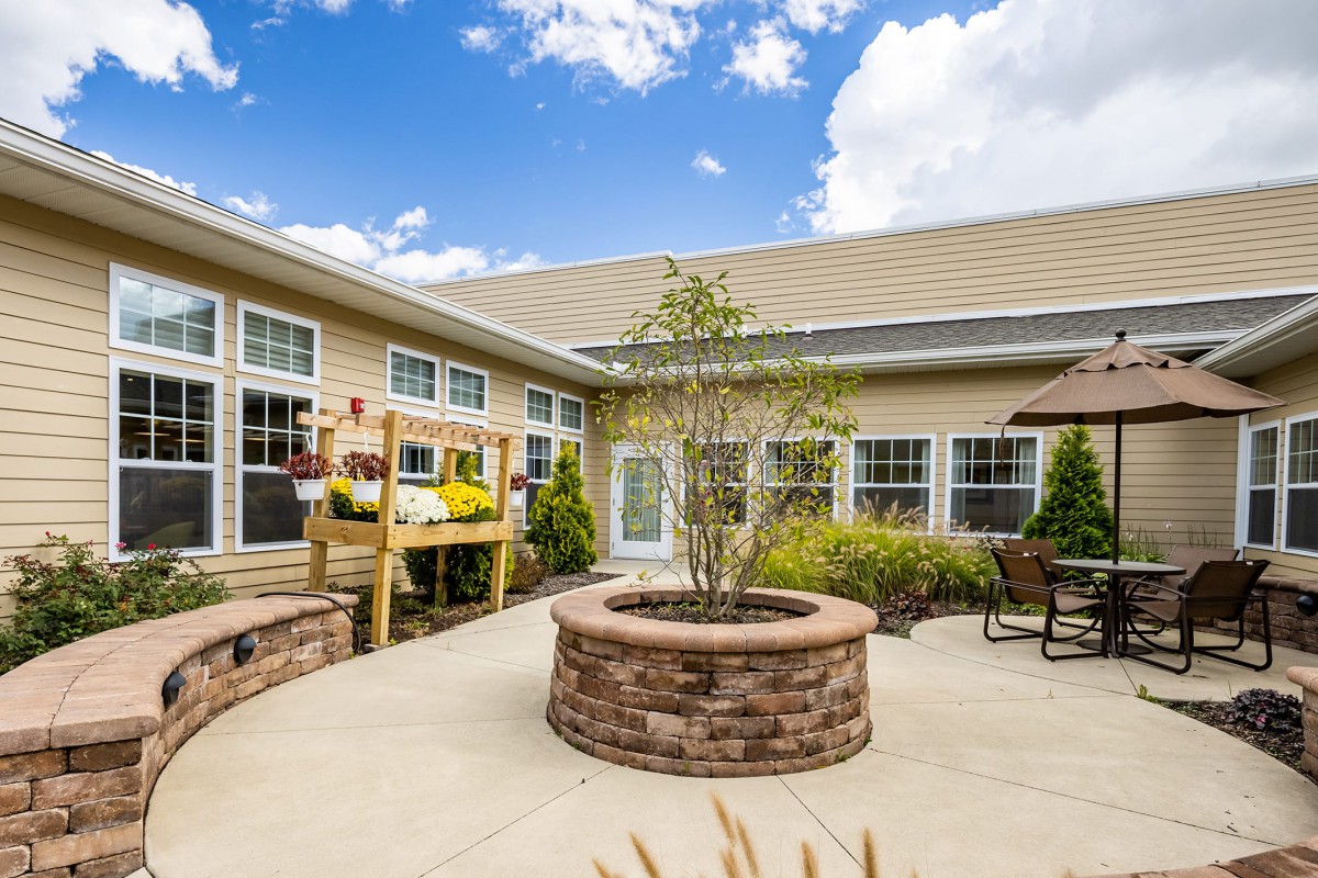A sunny courtyard featuring a brick planter, patio furniture, and vibrant landscaping.
