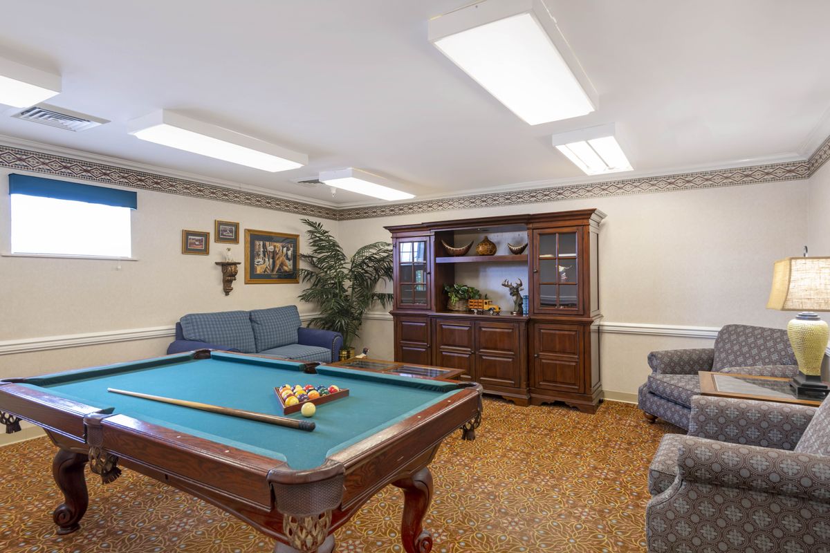 A cozy game room featuring a pool table, comfortable seating, and a large wooden cabinet.