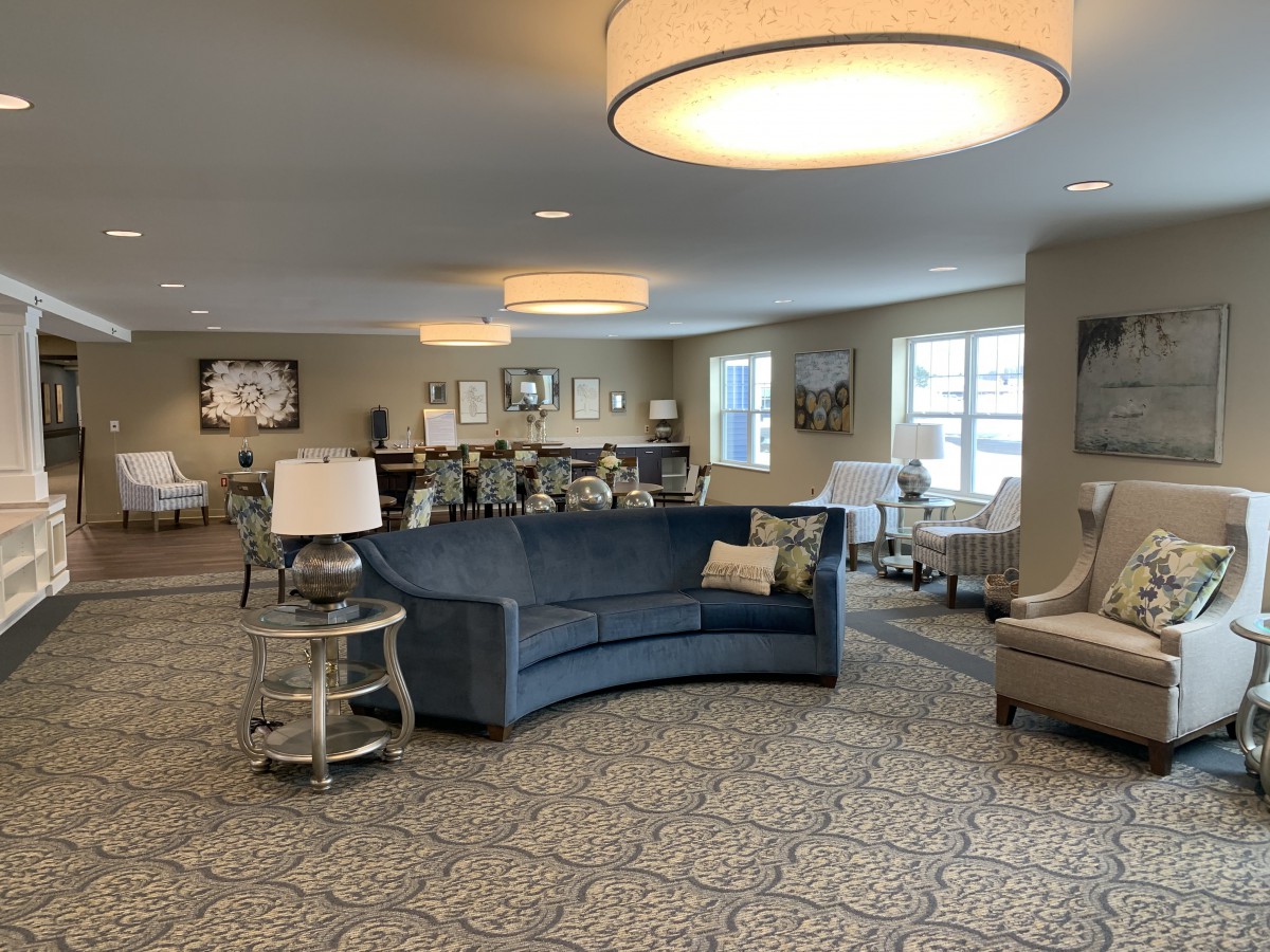 A spacious, well-lit living room featuring a curved blue sofa, round side table with lamps, and modern decor.