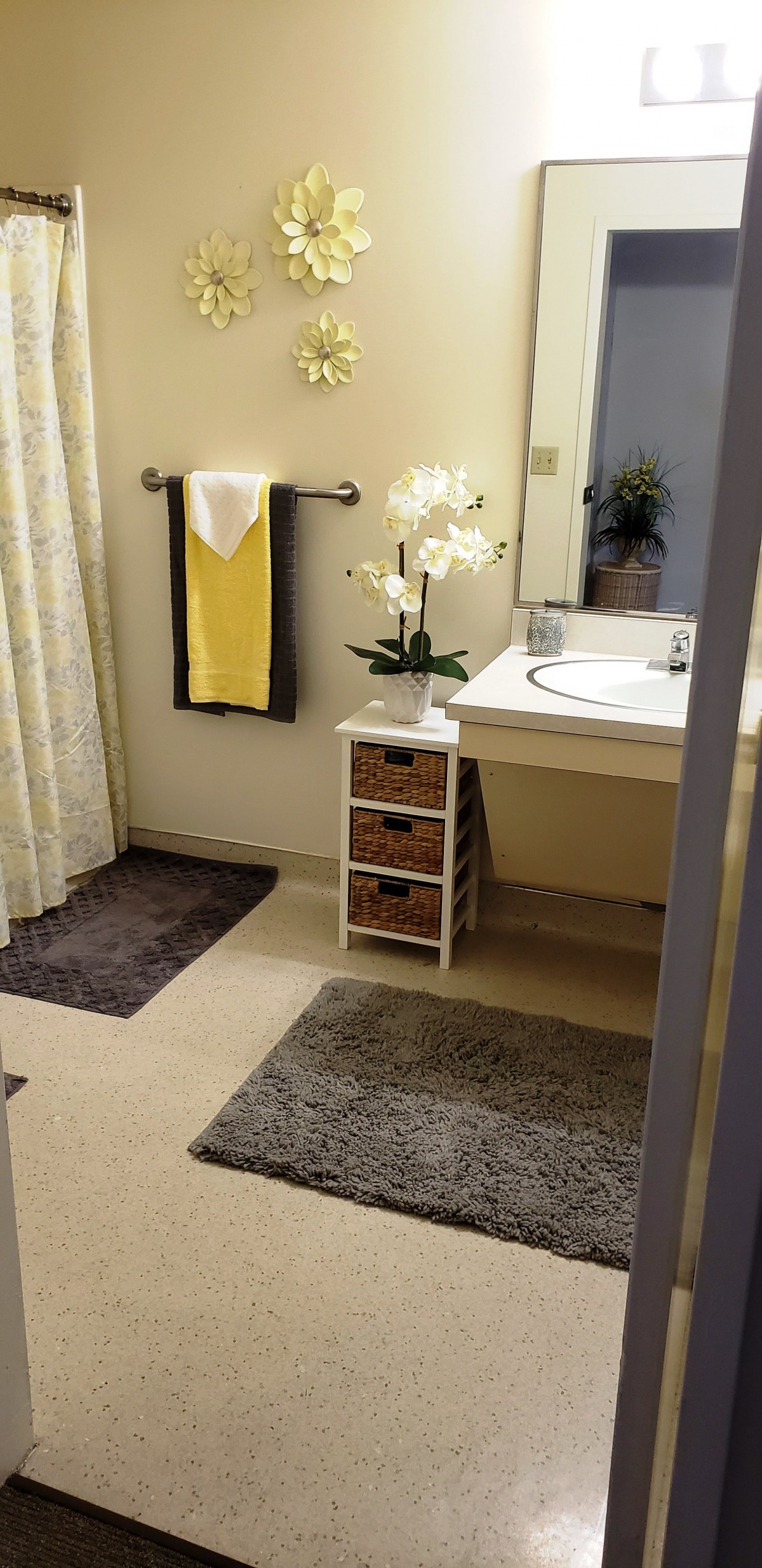A neatly organized bathroom with a yellow towel, plants, and decorative elements.