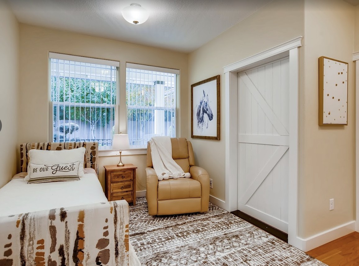 A cozy bedroom interior with a bed, armchair, and decorative rug.