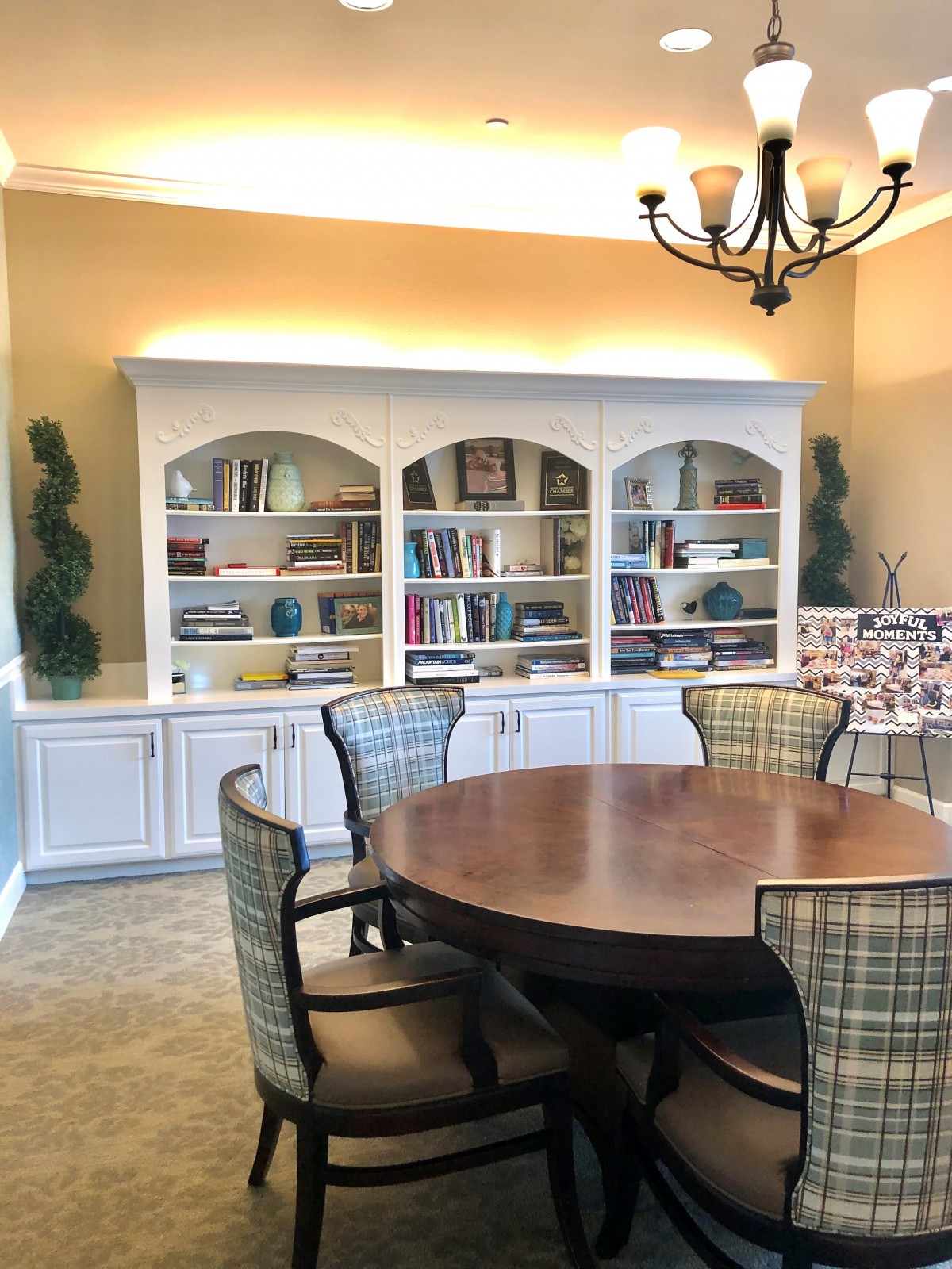 A cozy dining room with a round table, surrounded by chairs and a set of bookshelves in the background.