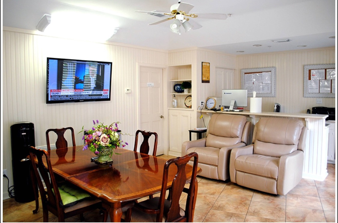 A cozy living space featuring a dining table with chairs, recliners, and a wall-mounted television.