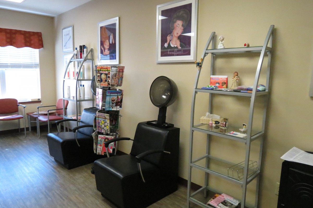 A cozy hair salon interior featuring a waiting area with chairs, magazines, and wall-mounted posters.