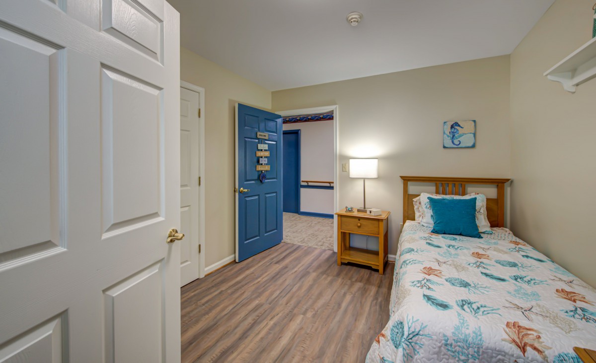 A cozy bedroom with a blue door, featuring a bed with floral bedding, a wooden nightstand, and soft lighting.
