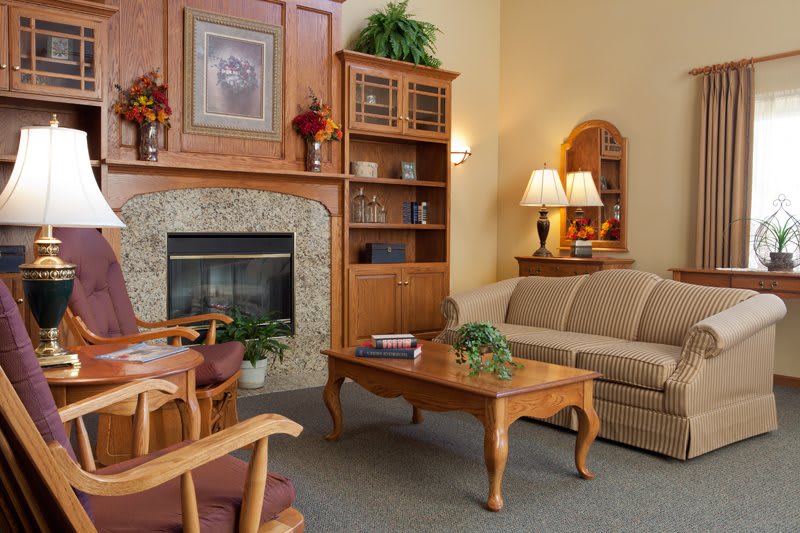 A cozy living room featuring comfortable seating, a central coffee table, and a warm fireplace surrounded by wooden furnishings.