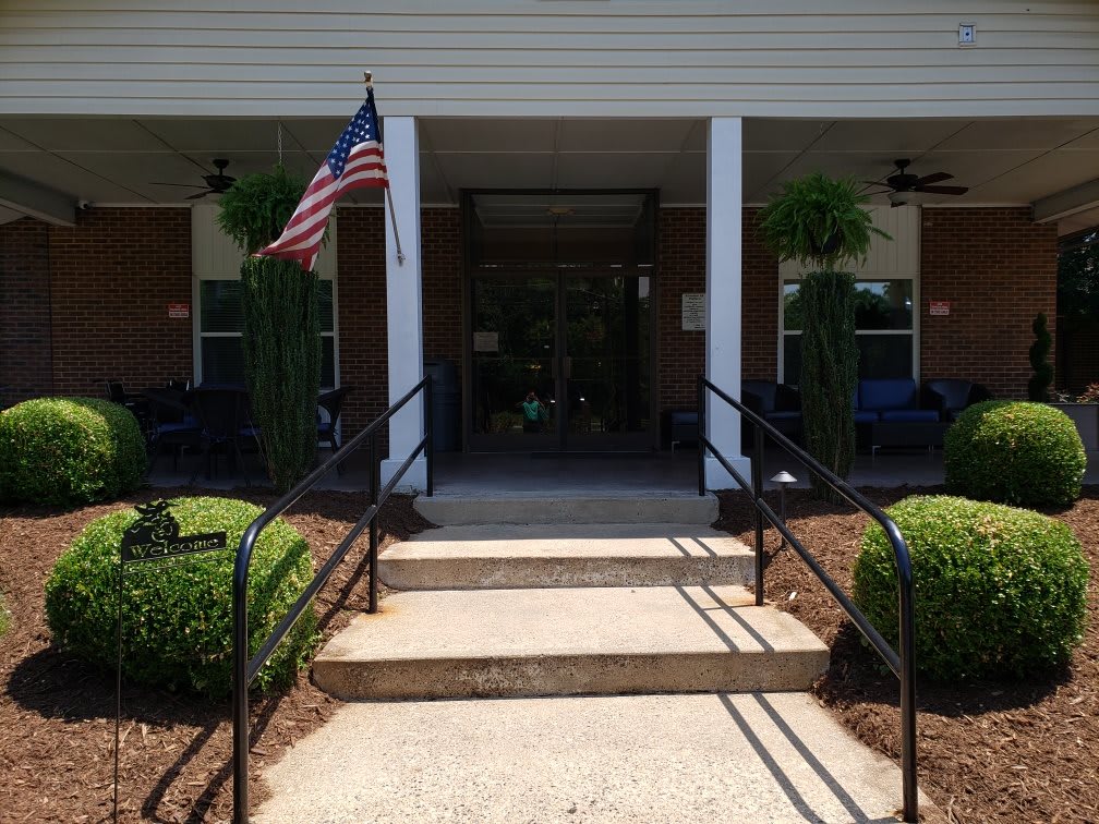Entrance to a building with an American flag and porch plants.