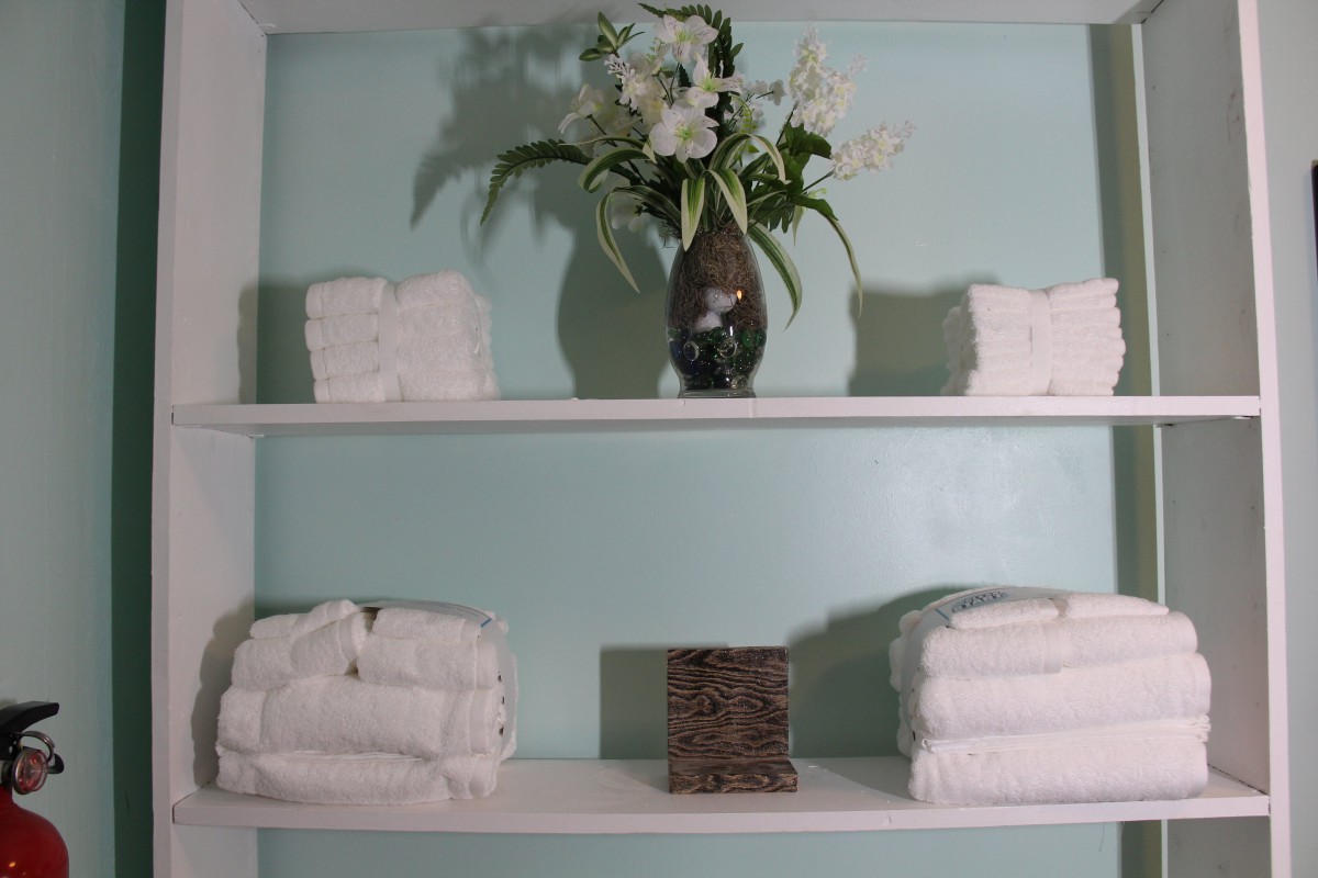 A neatly arranged bathroom shelf with folded towels and a vase of flowers.