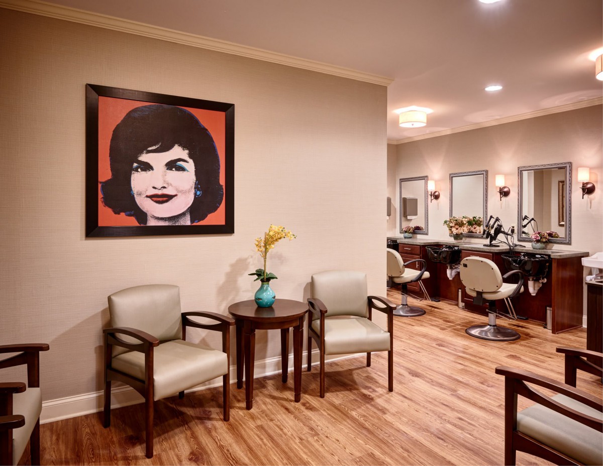 A salon interior with a waiting area featuring chairs, a table, and artwork on the wall.