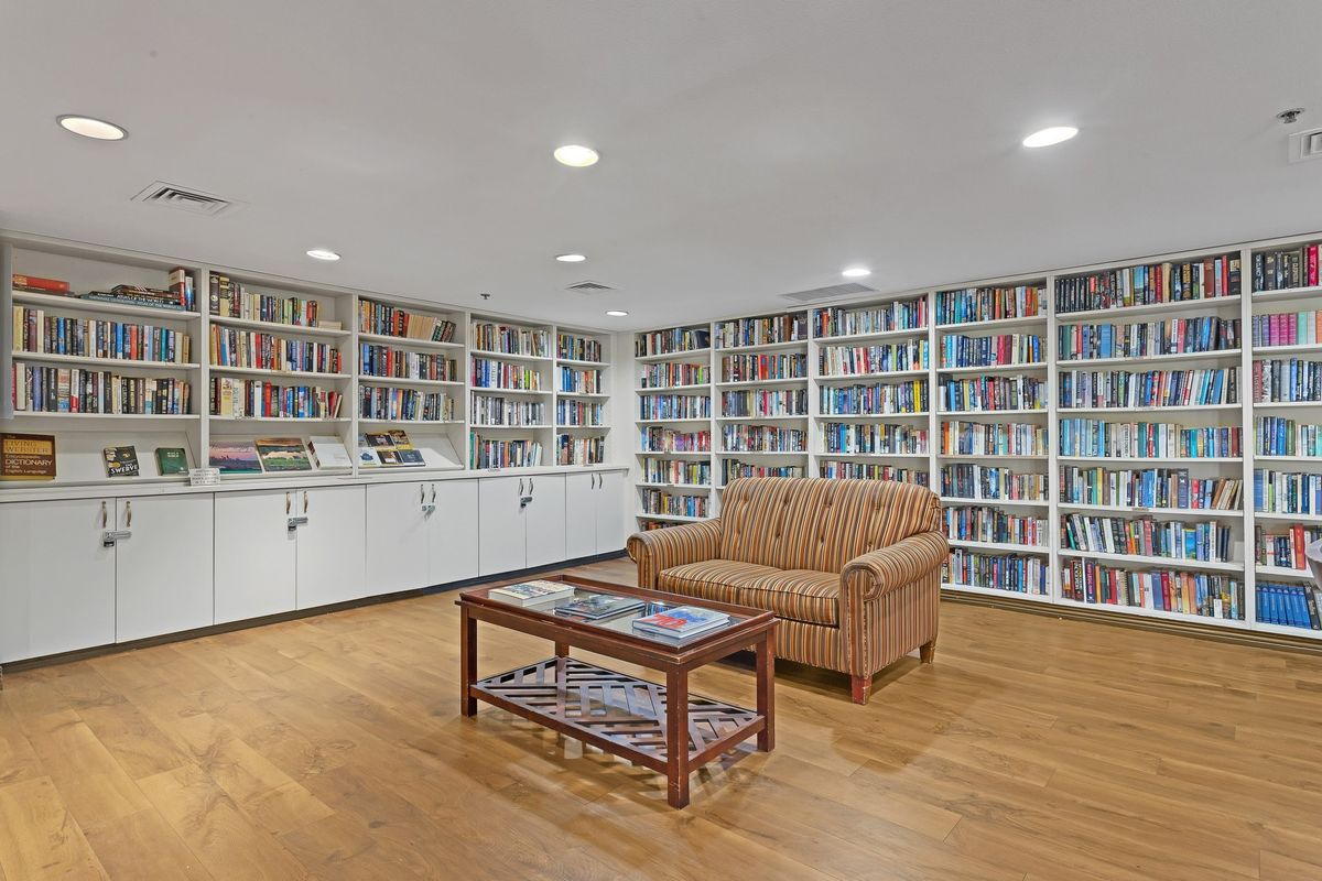 A cozy library with extensive bookshelves, a comfortable couch, and a wooden floor.
