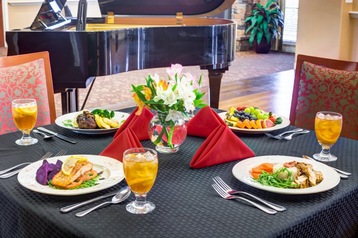 Elegant dining table setup with meals, red napkins, and a piano in the background.
