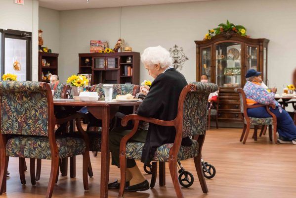 Elderly individuals sitting around a dining table in a nursing home setting, engaging in social activities.