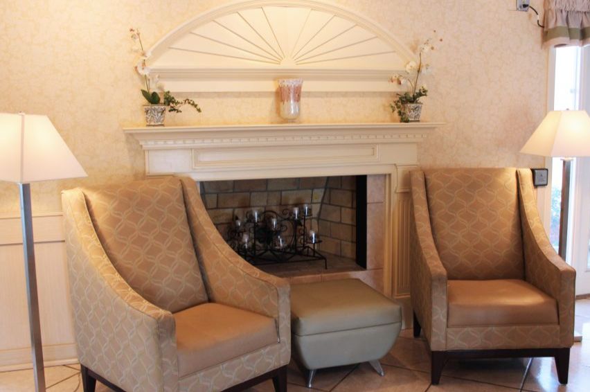 A cozy living room setting with armchairs flanking a decorative fireplace, adorned with plants.