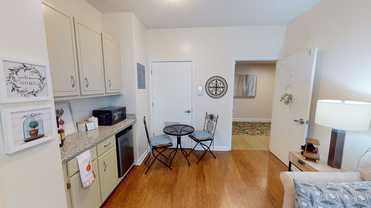 A small kitchen area with a table and two chairs, featuring wooden flooring and cabinets.