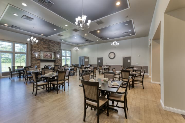 An elegant dining room with arranged tables and chairs, chandeliers, and a wooden floor.