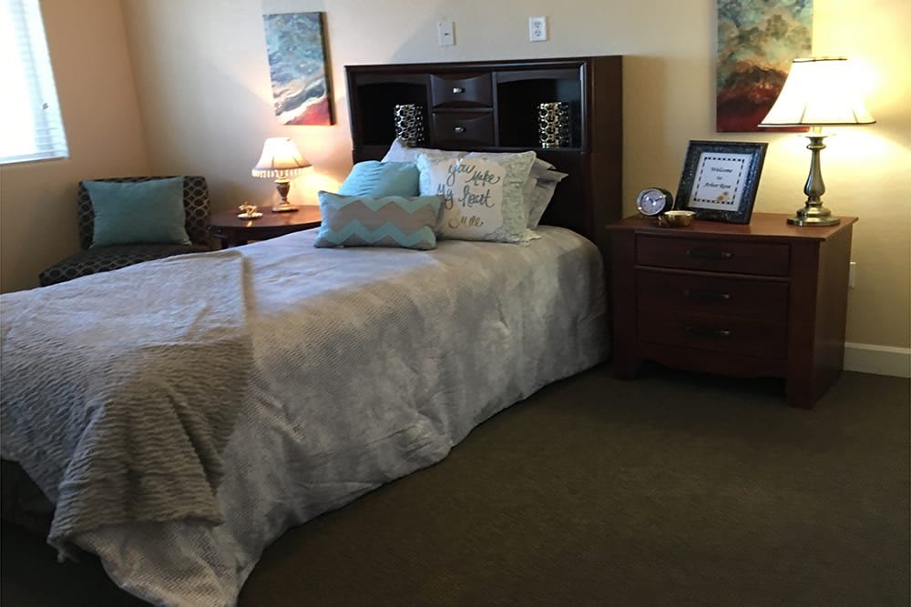 A cozy bedroom featuring a neatly made bed with multiple pillows, a nightstand with a lamp, and decorative artwork on the walls.