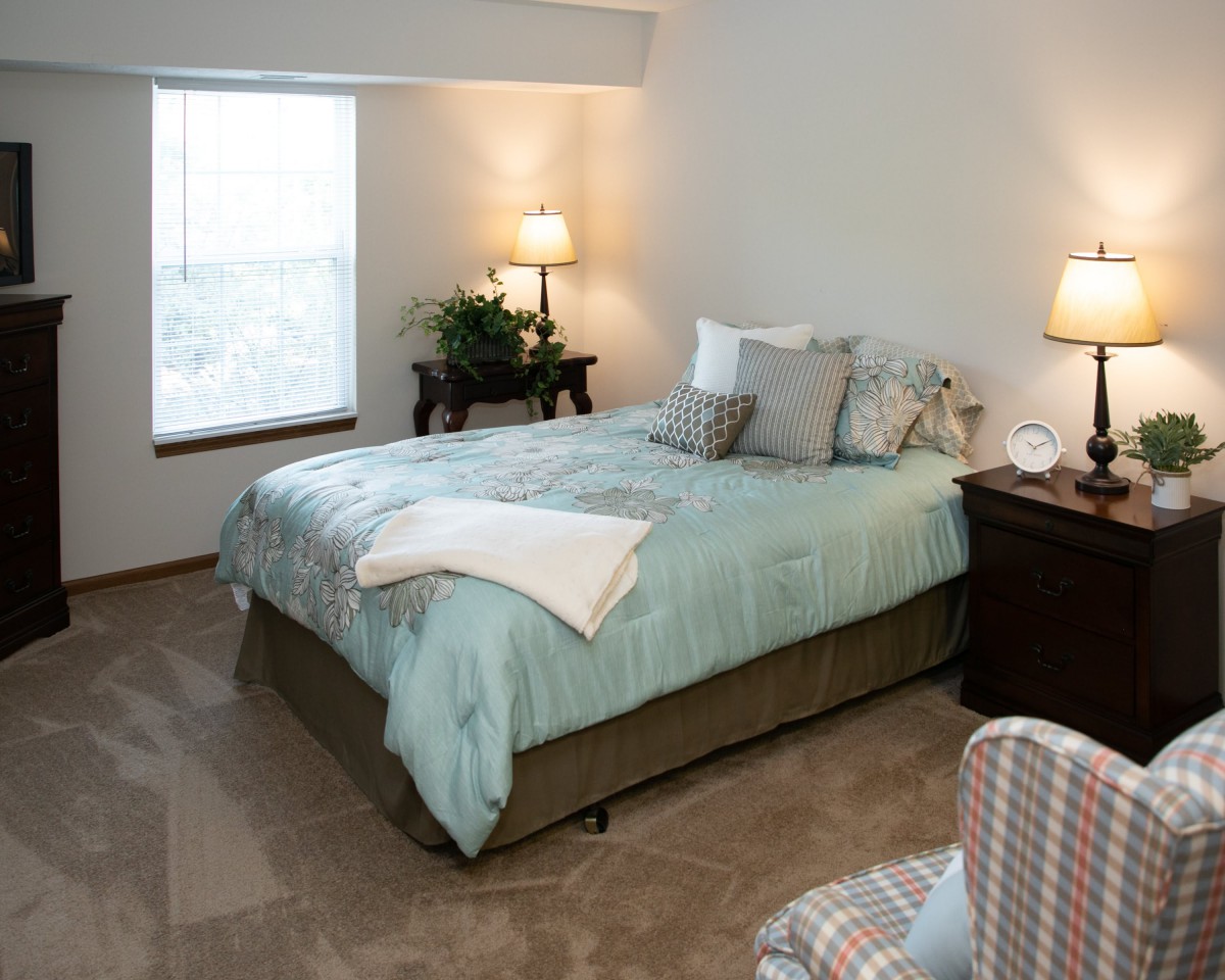 A cozy bedroom with a neatly made bed, soft lamps, and warm decor.