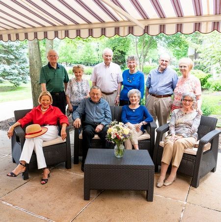 A group of seniors enjoying a gathering under a striped awning in an outdoor seating area.