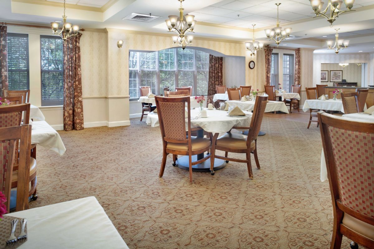 A spacious dining room with elegantly set tables and chairs, featuring chandeliers and large windows.