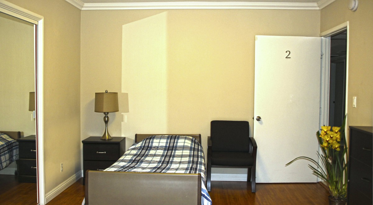 A simple bedroom with a bed, nightstand, lamp, chair, and door.