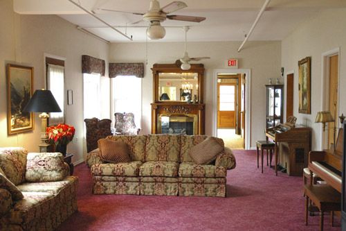 A cozy living room with a patterned sofa, carpeting, and a large mirror above the fireplace.