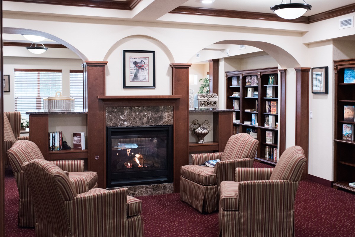 A cozy library with comfortable armchairs around a fireplace and bookshelves lining the walls.