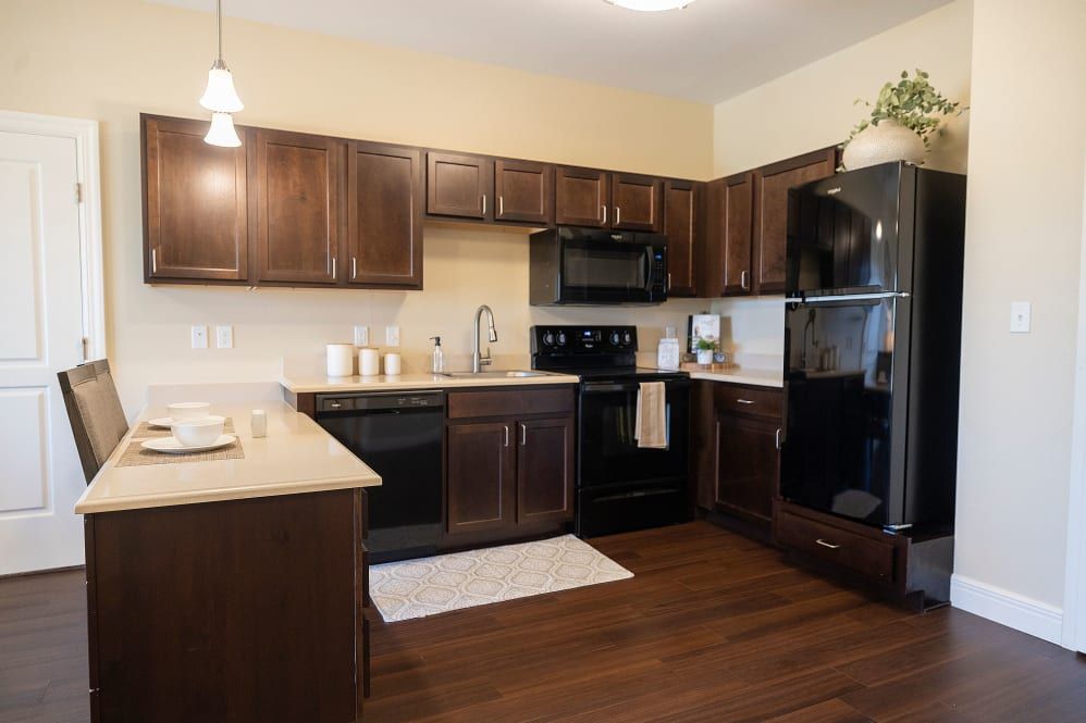 A modern kitchen with dark wooden cabinets, black appliances, and wood flooring.