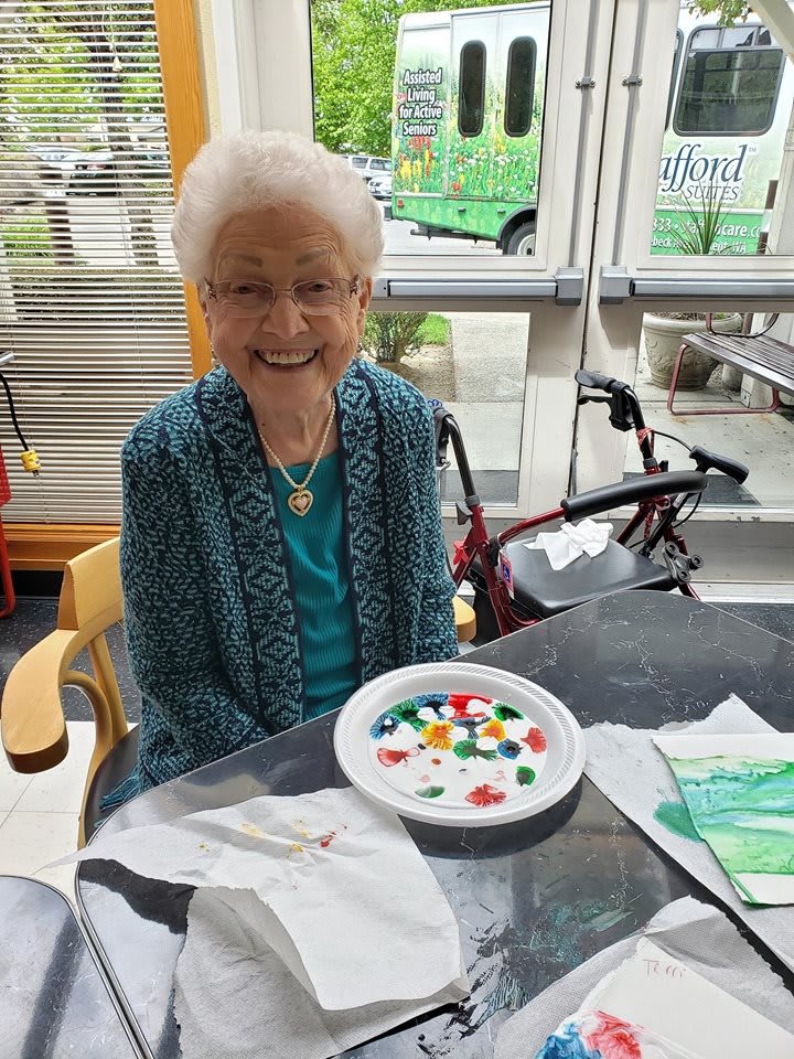 A smiling elderly woman sits at a table with a plate of colorful candies.