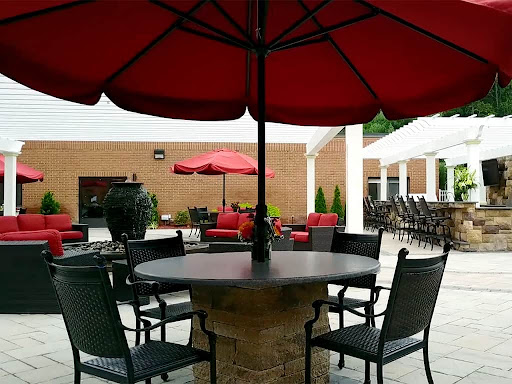 A serene outdoor patio setup featuring a round table with chairs under a vibrant red umbrella.