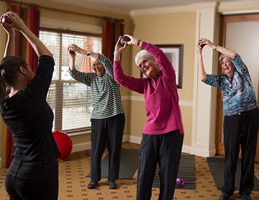 A group of seniors participating in an indoor exercise class, engaging in stretching activities.