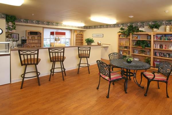 A cozy indoor space with a kitchen counter and bar stools, featuring wood flooring and decorated with shelves and plants.