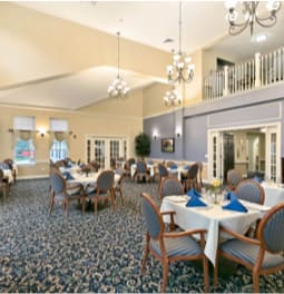 A spacious dining area with neatly arranged tables and chairs, elegant chandeliers, and a patterned carpet.