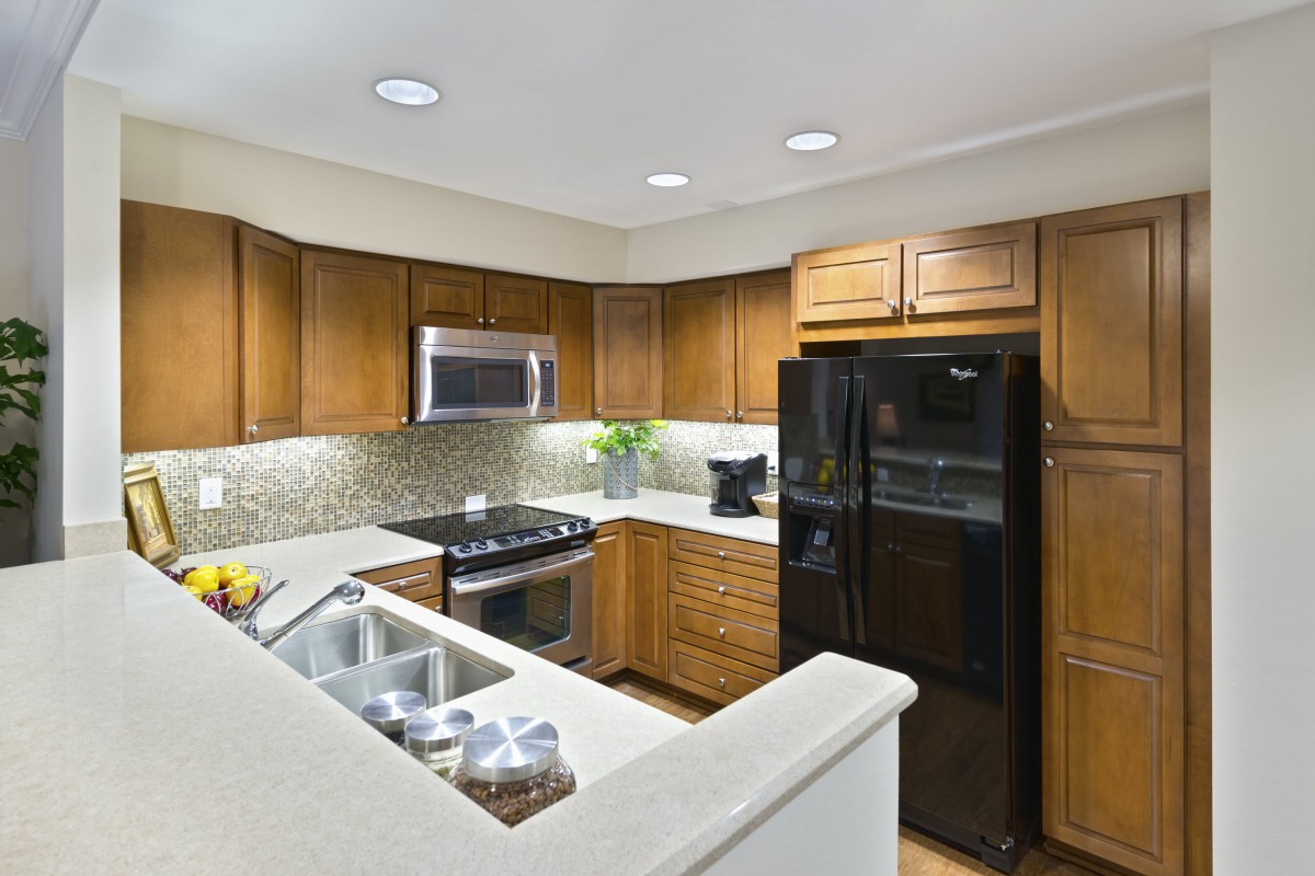 A modern kitchen with wooden cabinets, stainless steel appliances, and a black refrigerator.