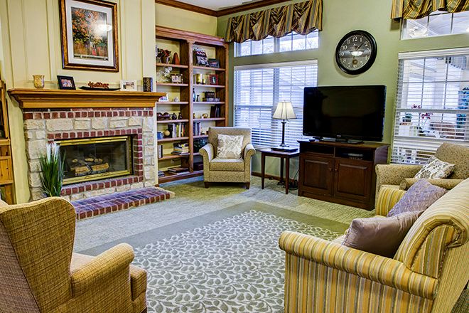A cozy living room featuring a fireplace, bookshelves, armchairs, and a television.