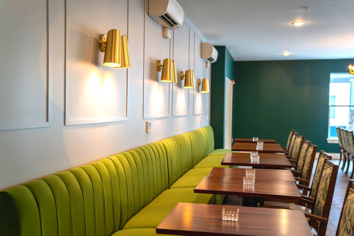 A modern restaurant interior with green upholstered seating, wooden tables, and stylish wall lighting.