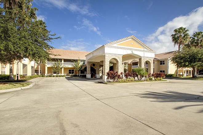 A view of a large building with an arched entrance and landscaped surroundings under a clear blue sky.