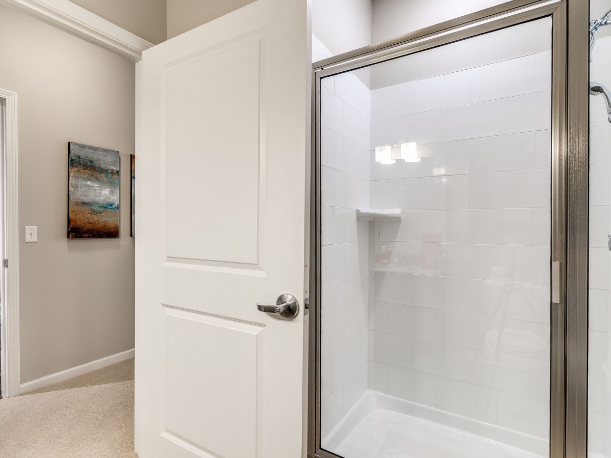 A modern bathroom with an open door revealing a white shower enclosure.