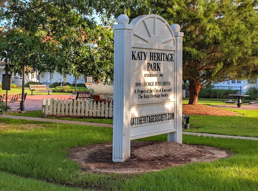 A historic sign marking a point of interest in Katy, Texas, surrounded by lush greenery.