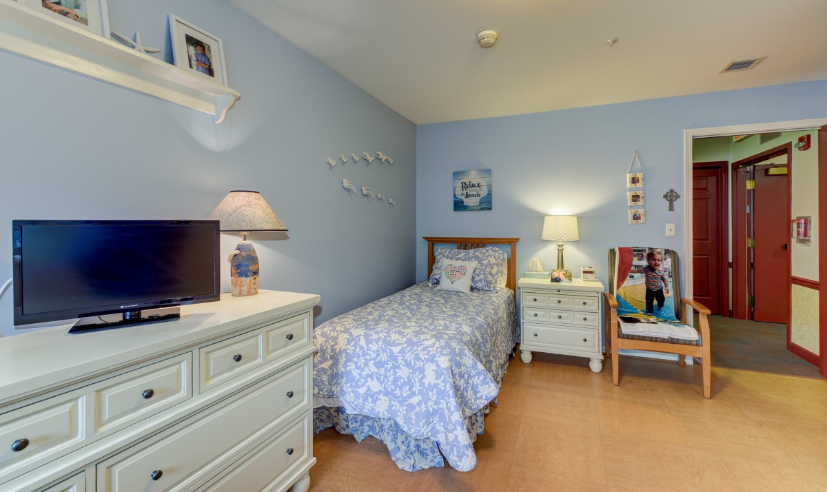A cozy bedroom with blue walls, featuring a single bed adorned with patterned bedding, complemented by a dresser and a nightstand with lamps.