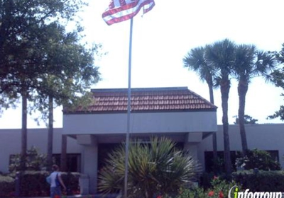 A view of a building with an American flag flying in front, surrounded by palm trees.