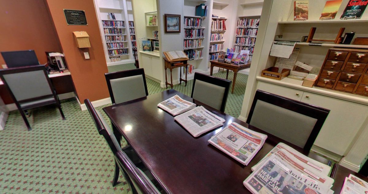 A cozy library reading area with newspapers on a table surrounded by bookshelves.